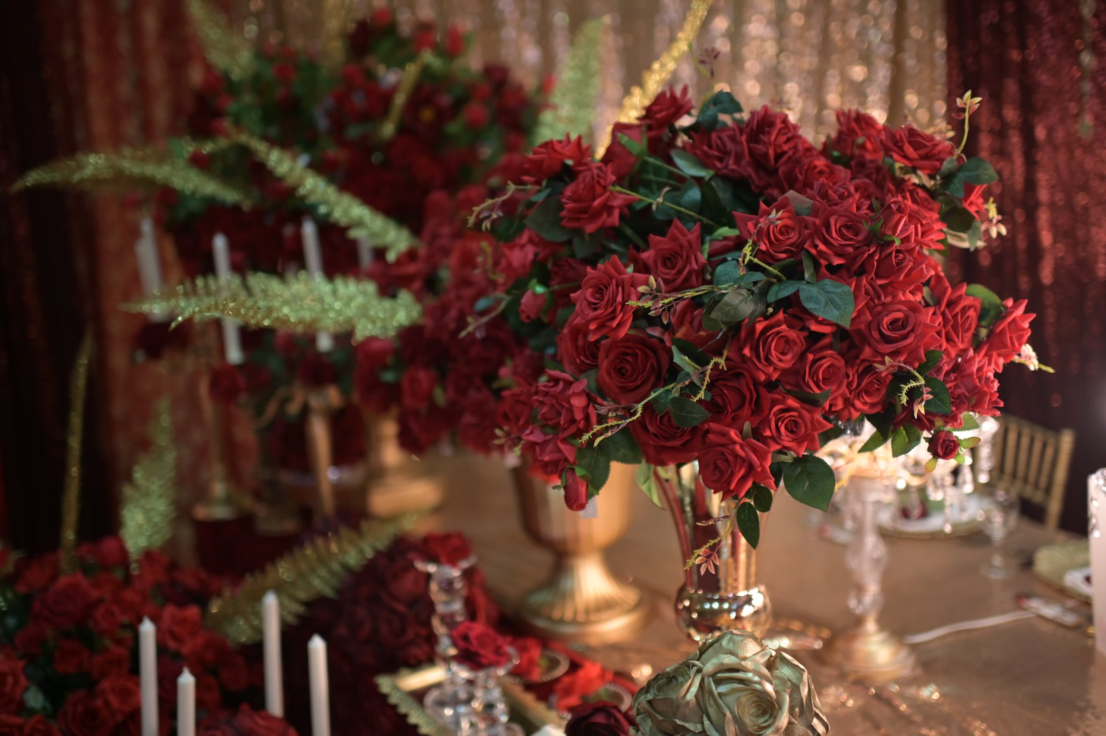 Deep red roses in a gold urn beside candles in The Royal Mirage collection.