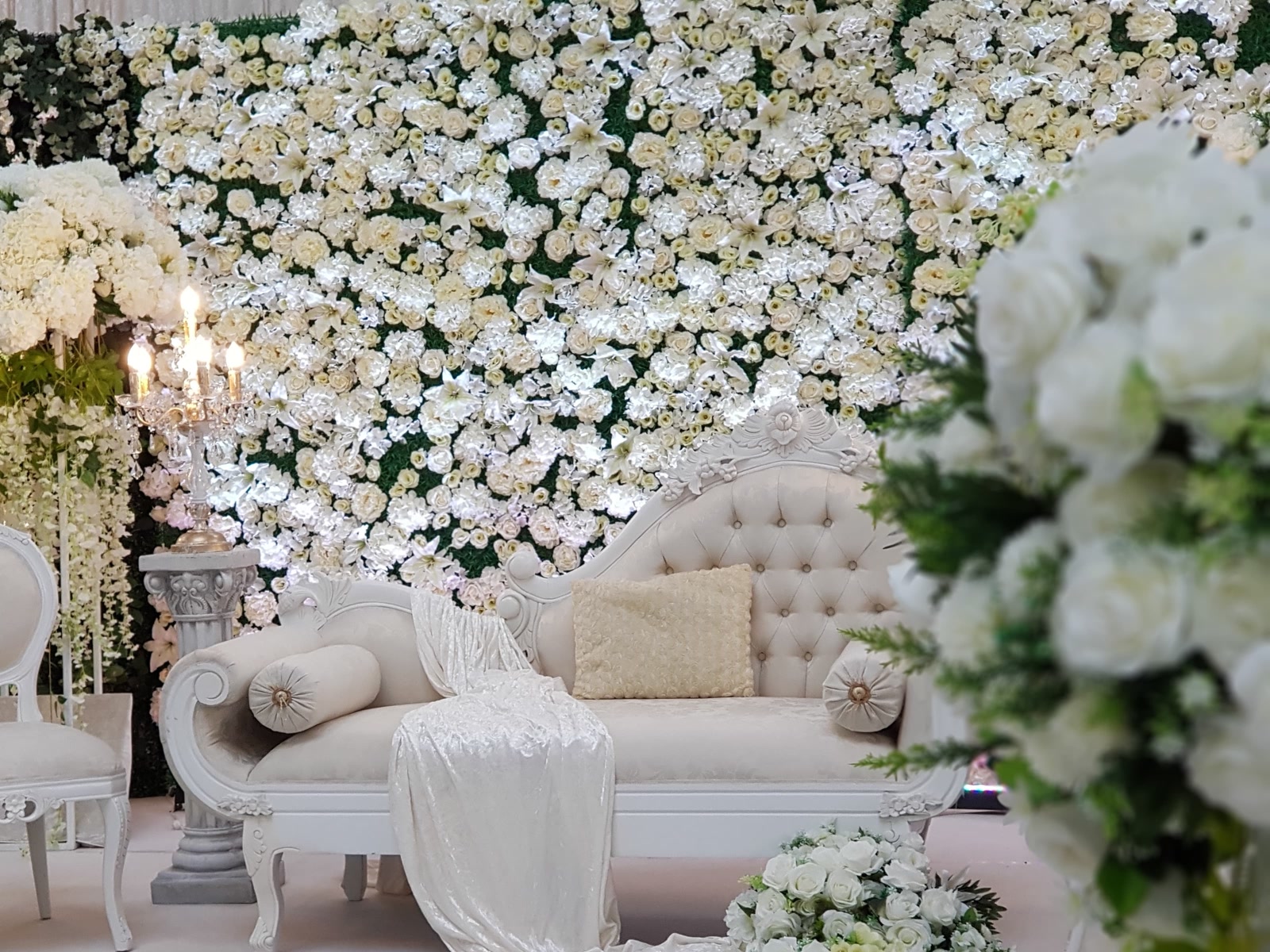 A wall of ivory roses behind a white carved sofa and crystal candelabra in The Royal Wedding Inspired collection.